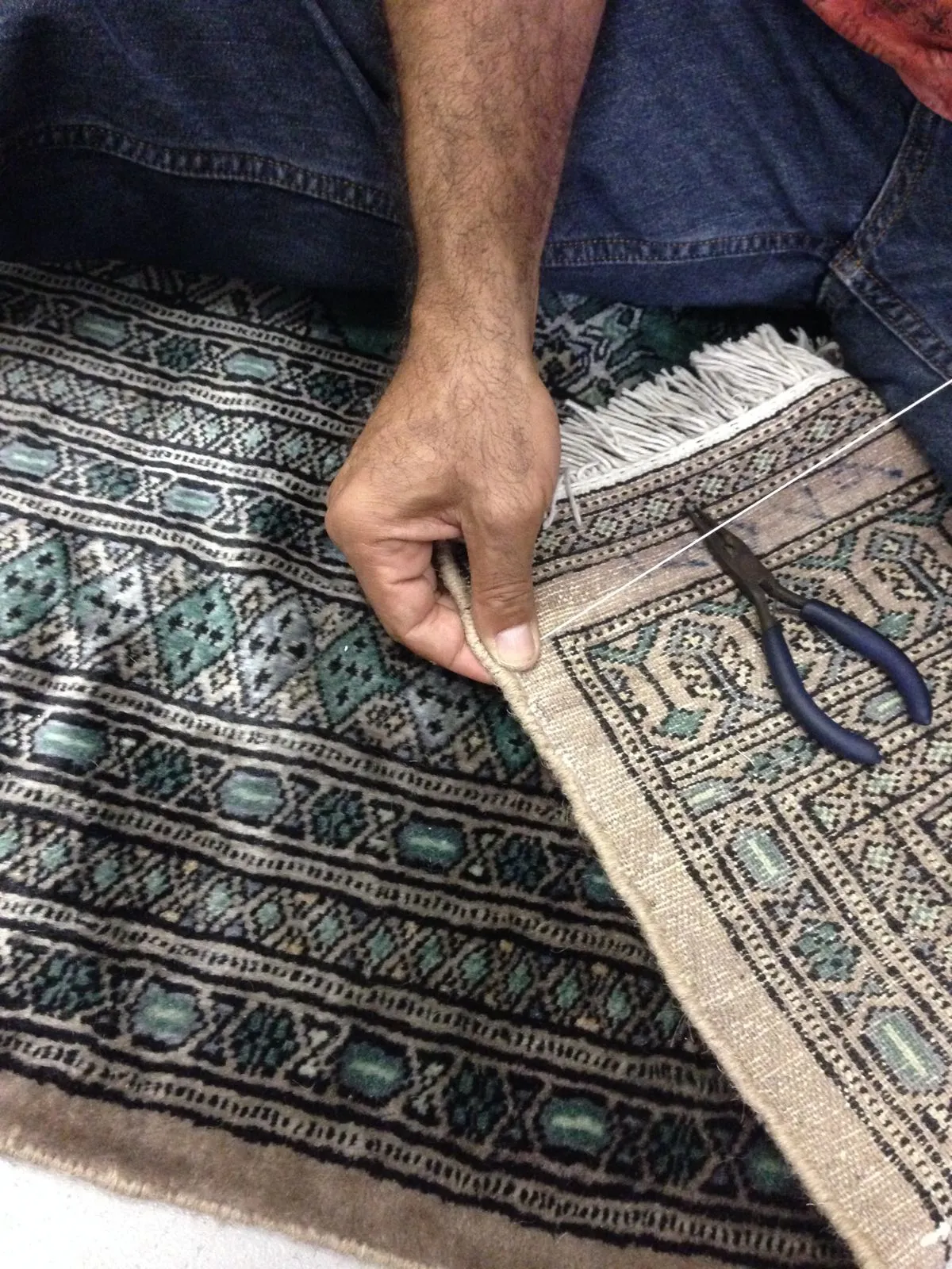 Close hand detail of a worn fringe being rebuilt at the repair bench