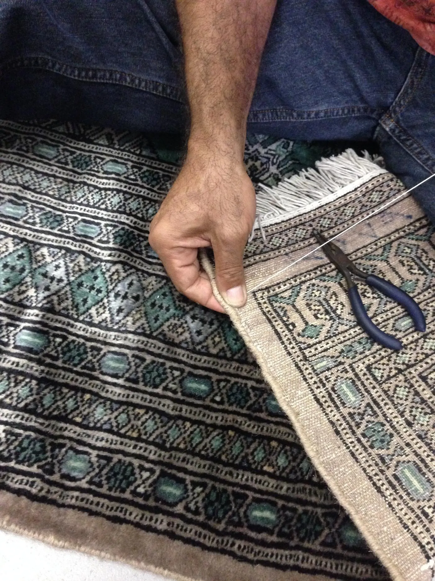 A rug's side edge being re-wrapped by hand with matched yarn
